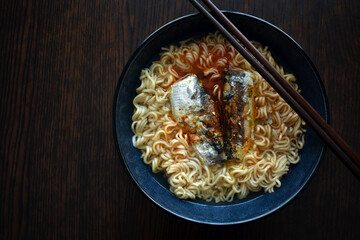 Instant noodles soup with sardine and seasoning with chopsticks in a black bowl. Copy space is on the left side.  Flat lay top view photo.