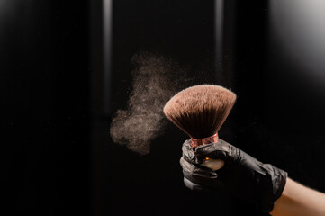 A woman shakes a large powder brush with clouds of dust on a black background. Treatment after...