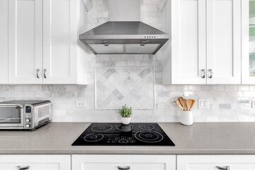 Detail shot of a white luxurious kitchen stove and hood. A marble custom tile back splash is under...