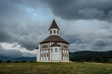 Small white rural Tesarovska chapel with cemetery in village of Korenov, Jizera mountains, Czech Republic. Summer landscape, stormy sky.Wooden historic church. Religious scenery.Czech countryside
