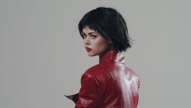 A woman dances in a stylish fashion red cloak with a beautiful make-up with black short hair in front of the camera