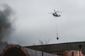 A fire helicopter carries a container of water to extinguish a fire in a production building
