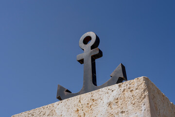 Czarna morska kotwica na betonowym murze na tle niebieskiego nieba. © Aneta