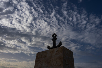 Czarna morska kotwica na betonowym murze na tle niebieskiego nieba. © Aneta