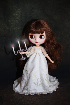 Blythe doll in long white dress with candlestick on dark background - Saint Petersburg, Russia, August 2022