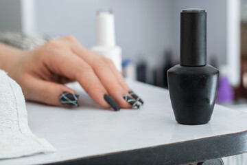 close-up of matte black nail polish on a white manicure table, in the background a hand with black painted nails. concept of beauty and dark style.
