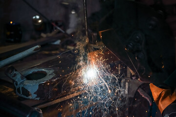 Welding old metal car part at workshop, sparks and smoke flying around, closeup detail