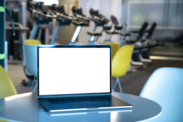 Laptop with white screen in fitness center in shopping mall. Empty copy space, blank screen mockup. Soft focus laptop with interor background. Healthy, gym and yoga concept