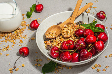Summer breakfast concept. Healthy morning food. Ripe cherries and granola, light concrete background