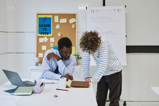 Portrait of young black teacher helping boy with task or grading homework in school classroom