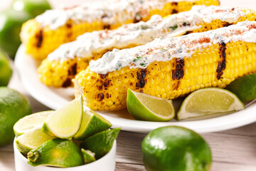 Elote on a white plate, grilled mexican street corn, roasted cobs are slathered in sour cream based...