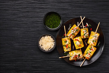 Grilled corn on cob sprinkled with cilantro and grated parmesan in a black plate on a table,top view.