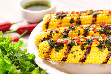 Plate with grilled corn on cob sprinkled with cilantro and chilli pepper on light background, selective focus.