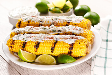 Elotes, grilled mexican street corn, roasted cobs are covered in creamy mayonnaise, seasoned with chili powder and cilantro and  lime close up.