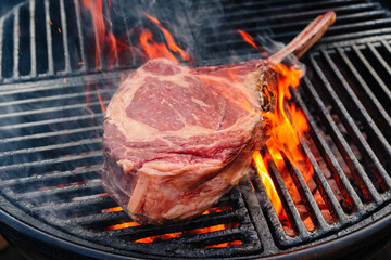 Barbecue dry aged wagyu tomahawk steak offered as close-up on a charcoal grill with fire and smoke