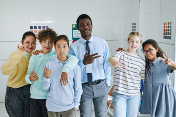 Portrait of smiling teacher posing with diverse group of children and showing hand signs