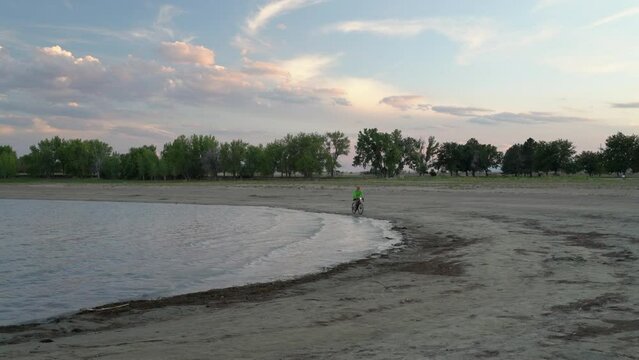 senior male is riding a gravel bike on a beach at summer dusk, Boyd Lake State Park in Loveland, Colorado