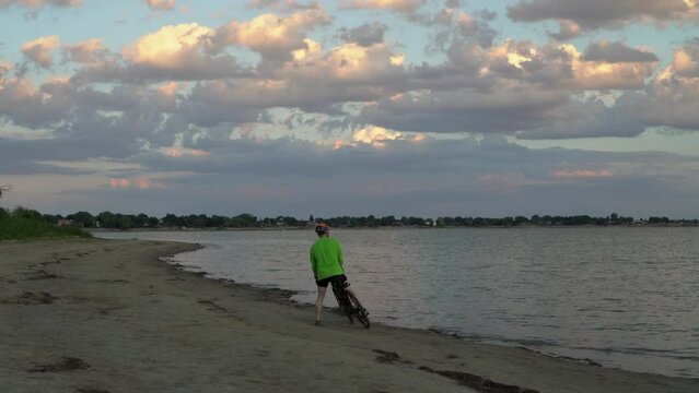 senior male is riding a gravel bike on a beach at summer dusk, Boyd Lake State Park in Loveland, Colorado