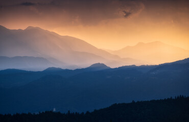 Amazing silhouettes of a mountains at colorful sunset in summer in Slovenia. Landscape with mountain ridges in fog, golden sunlight and clouds in the evening. Nature. Hills in sunlight. Scenery