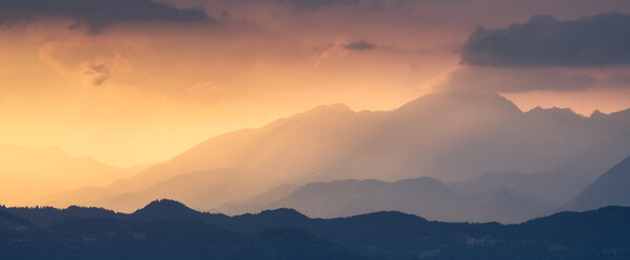 Obraz na płótnie Canvas Amazing silhouettes of a mountains at colorful sunset in summer in Slovenia. Landscape with mountain ridges in fog, golden sunlight and clouds in the evening. Nature. Hills in sunlight. Scenery