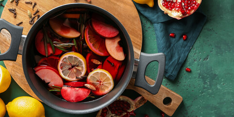 Saucepan of delicious mulled wine on green background, top view