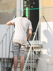 A caucasian guy in gray sports and a T-shirt from the back washes metal a ladder up