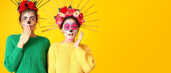 Surprised women with painted skull on faces against yellow background with space for text. Halloween celebration