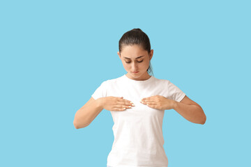 Young woman suffering from breast pain on blue background