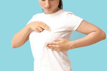 Young woman suffering from breast pain on blue background, closeup