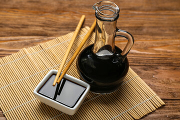 Bowl and jug of soy sauce, chopsticks with bamboo mat on wooden background