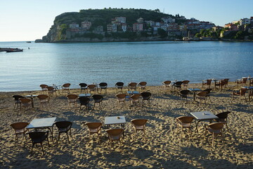 Leere Tische und Stühle am Strand im Sommer im Licht der Abendsonne in der Bucht an der Küste von...