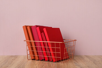 Metal basket with books on table near pink wall