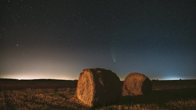 Comet Neowise C 2020 F3 In Night Starry Sky Above Haystacks In Summer Agricultural Field. Night Stars Above Rural Landscape With Hay Bales After Harvest. Agricultural Concept. 4K Timelapse.