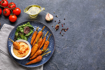 Composition with plate tasty baked carrots, sauce and spices on dark background