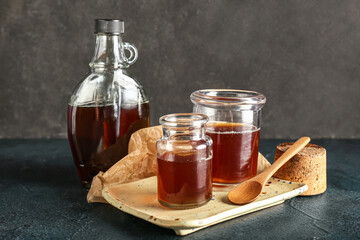 Bottle and jars of tasty maple syrup on dark background