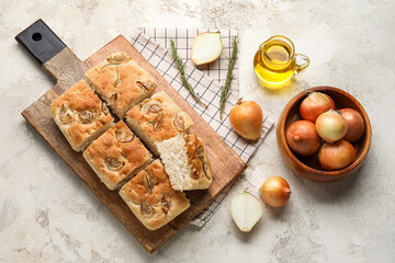 Wooden board with tasty Italian focaccia, bowl of onion and oil on light background