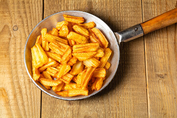 French fries on old pan placed on wooden table.