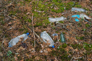 Obraz premium Plastic garbage in forest. Used disposable plastic bottles, containers and glass bottles in forest clearing. Pollution environment. Long decaying waste in nature