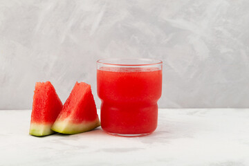 Watermelon smoothie or watermelon juice in clear glass on grey background. Near lie juicy slices with red pulp. Jus semangka. Selective focus, space for text