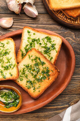Plate of toasts with garlic and parsley on wooden table, closeup