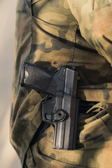 Vertical close-up shot of handgun in holster around soldier's waist. Camouflage army uniform. ....