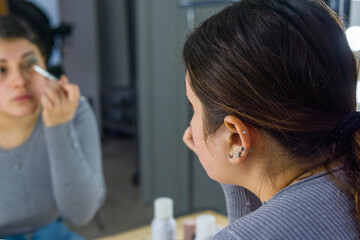 close-up rear view of a woman brushing her eyelid while looking in a mirror during a makeup process