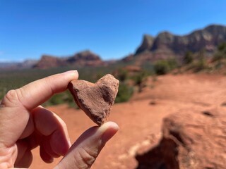 Close up of hand holding up a natural heart-shaped red rock on a Sedona hiking trail