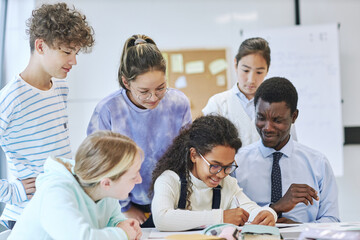 Fototapeta premium Diverse group of children smiling happily in school while working together with young male teacher