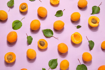 Many ripe apricots and leaves on pink background