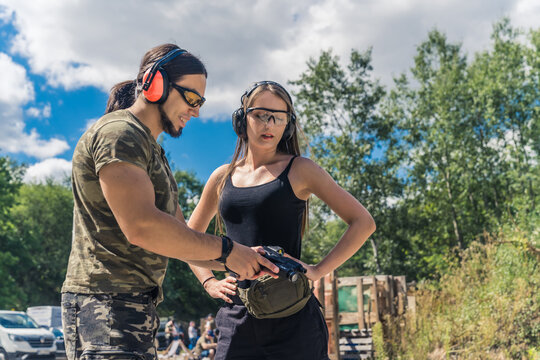 Caucasian man and woman wearing safety goggles and headphones learning how to operate handgun. Firearms training at firing range. Horizontal outdoor shot. High quality photo