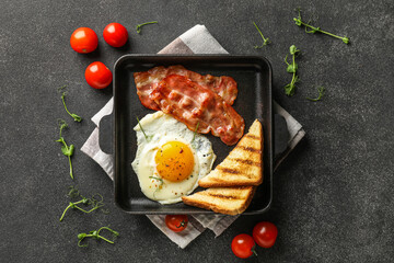 Composition with frying pan of tasty fried egg, bacon, toasts and tomatoes on dark background