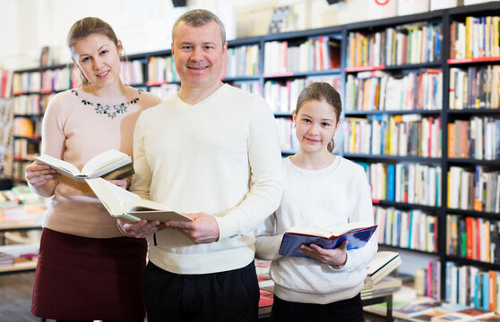 Smiling family with preteen daughter reading interesting books in bookshop