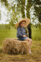 Dziewczynka z kapeluszem siedzi na słomie na farmie - obrazy, fototapety, plakaty