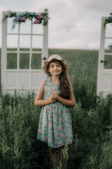Młoda kobieta w sukience i kapeluszu trzyma w dłoniach polne kwiaty